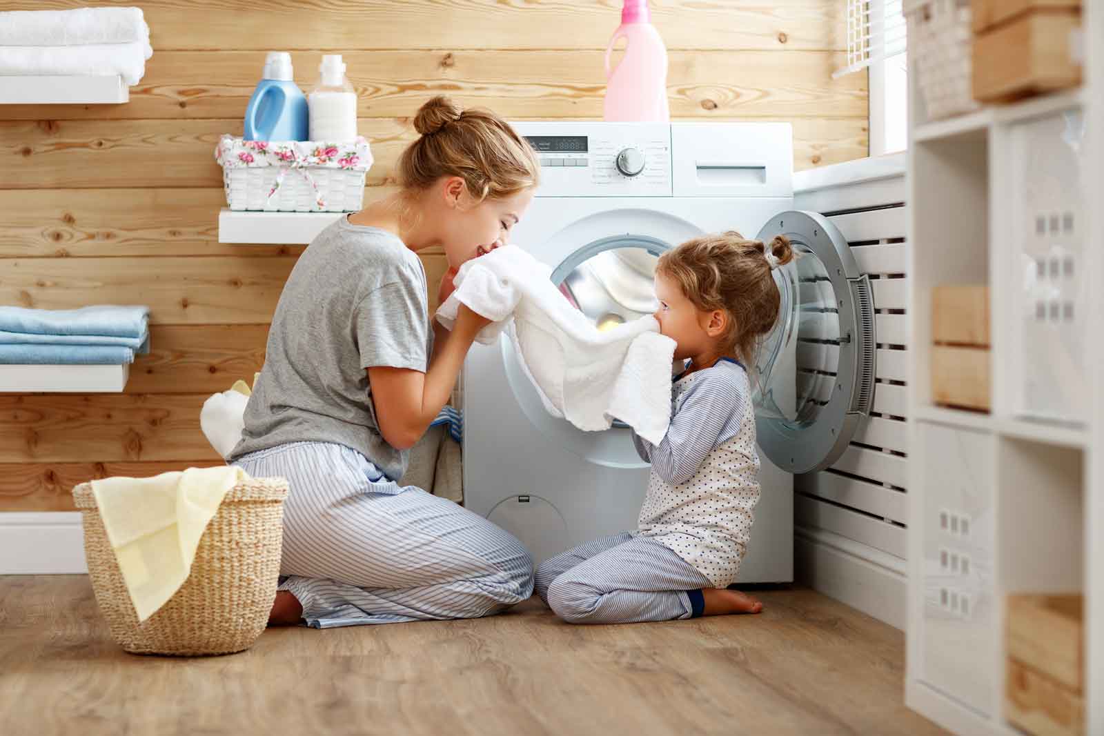 A woman and her daughter are sitting in front of a washing machine.