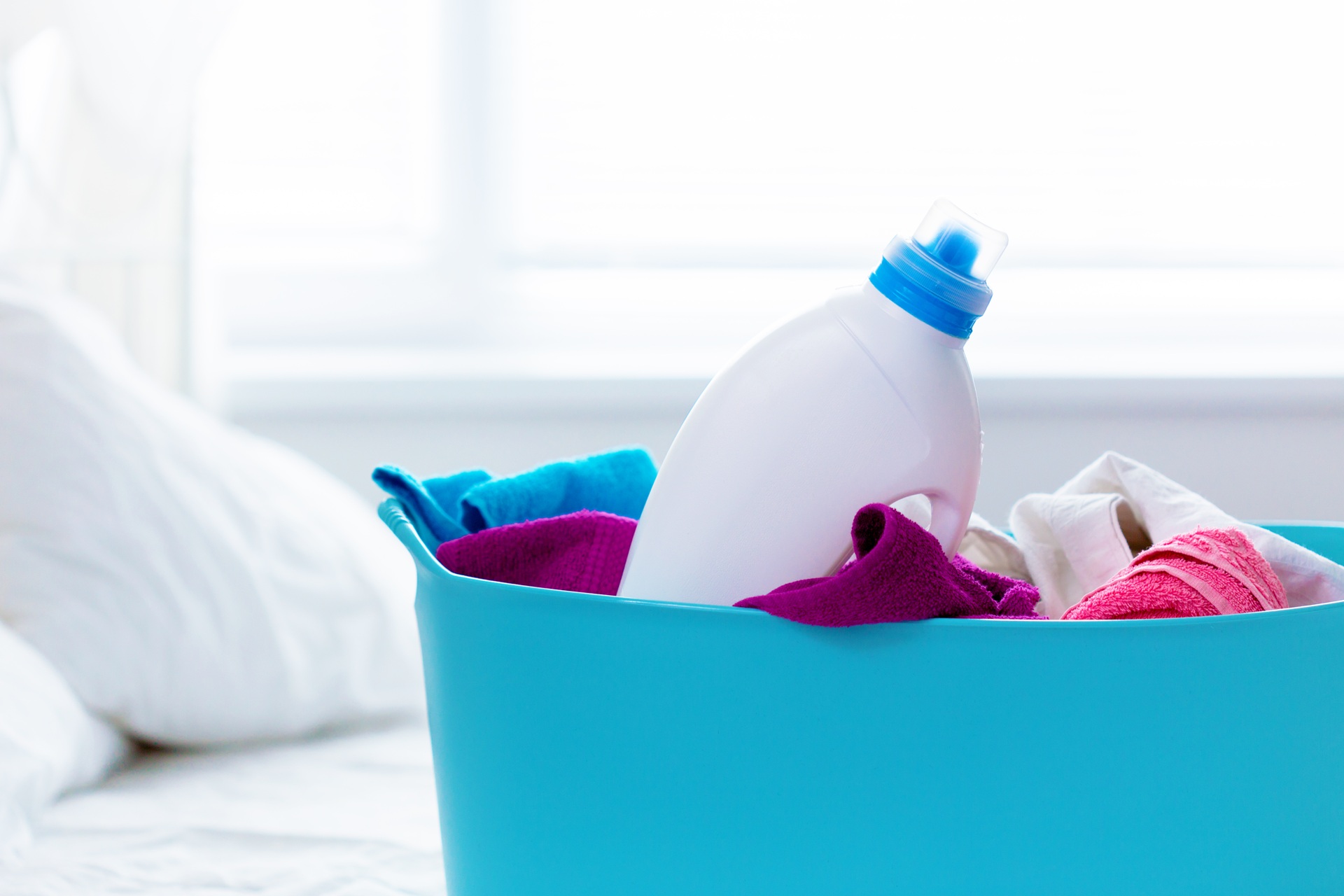 A blue laundry basket containing various colorful towels and a white bottle of detergent.