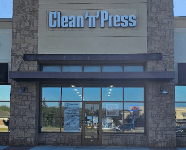 A storefront with stone facade displays "Clean 'n' Press" sign. Large front windows show "Now Hiring" and "Open" signs.