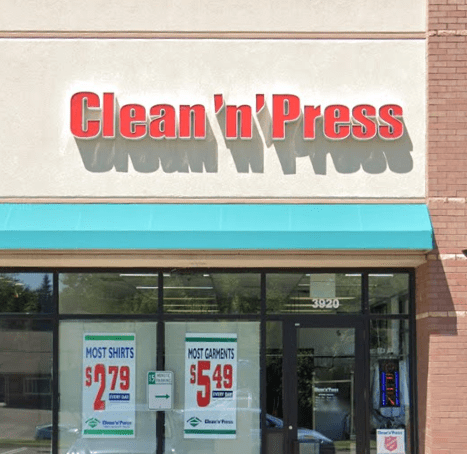 Storefront of Clean 'n' Press with promotional signs reading "Most Shirts $2.79" and "Most Garments $5.49" displayed in the windows.
