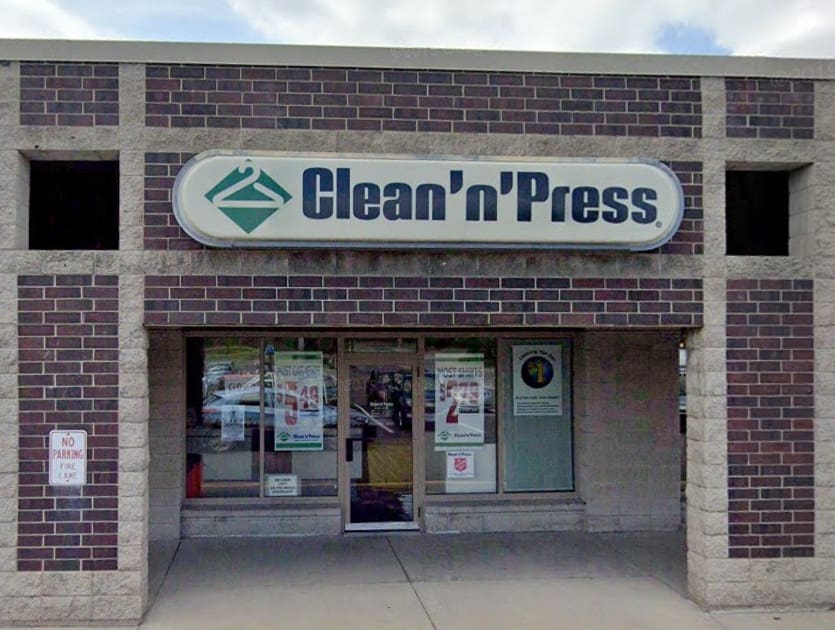 Storefront of a dry cleaners with a sign reading "CLEANERS." The door is open, displaying signs for free pickup and delivery. An "OPEN" sign is in the window.
